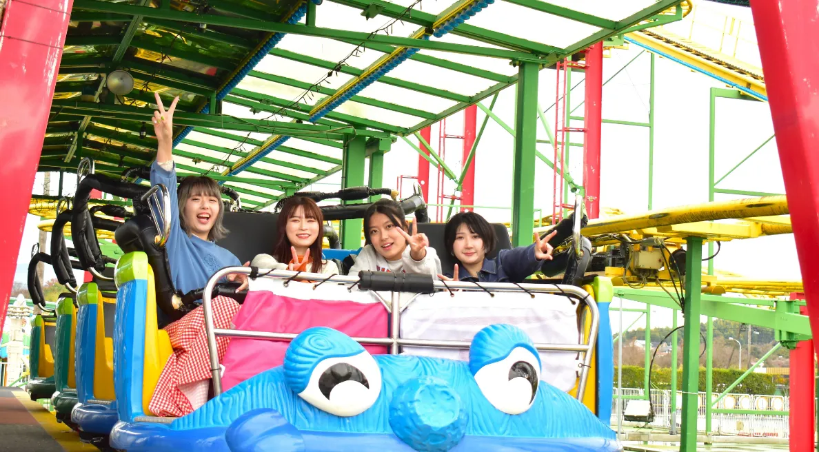 写真：4人横並びに座れる席になっている、ジェットコースターの最前列に座ってピースサインを出している4人の女性グループ